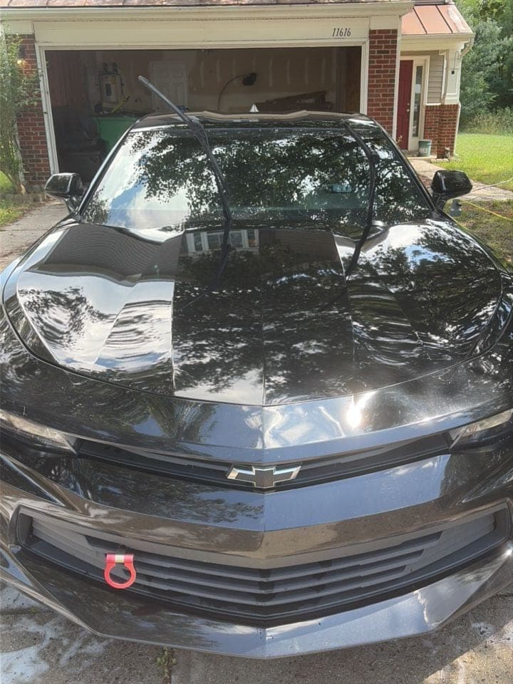 Black Chevrolet Camaro in a driveway after a full exterior detail, paint and glass gleaming
